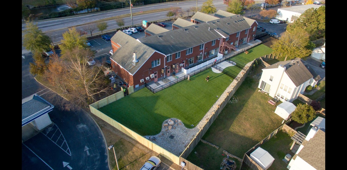 Aerial view of fenced dog exercise areas, turf, and curved concrete paths within an existing developed site