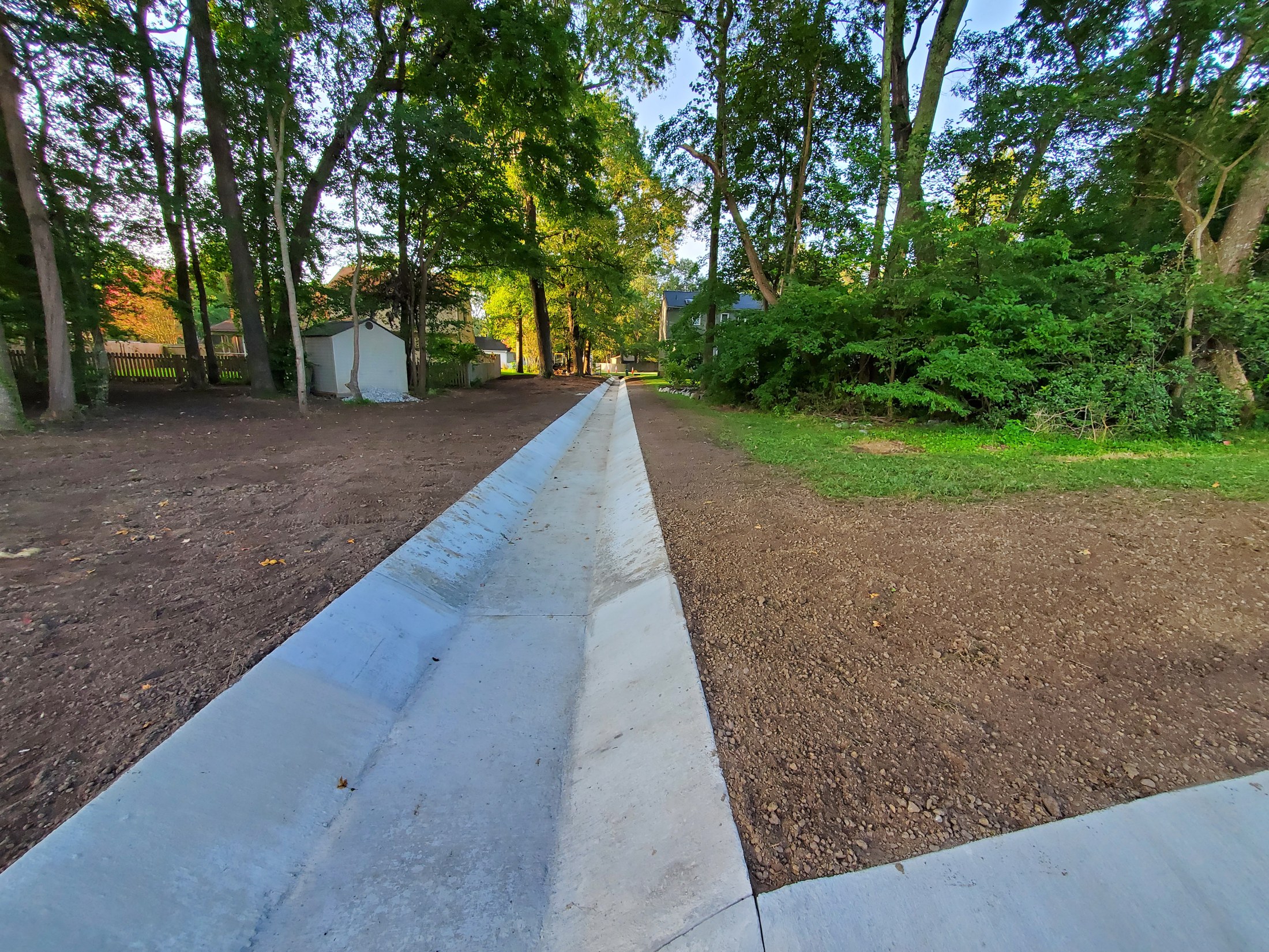 Completed concrete channel extending through a wooded site, with surrounding ground prepared for restoration