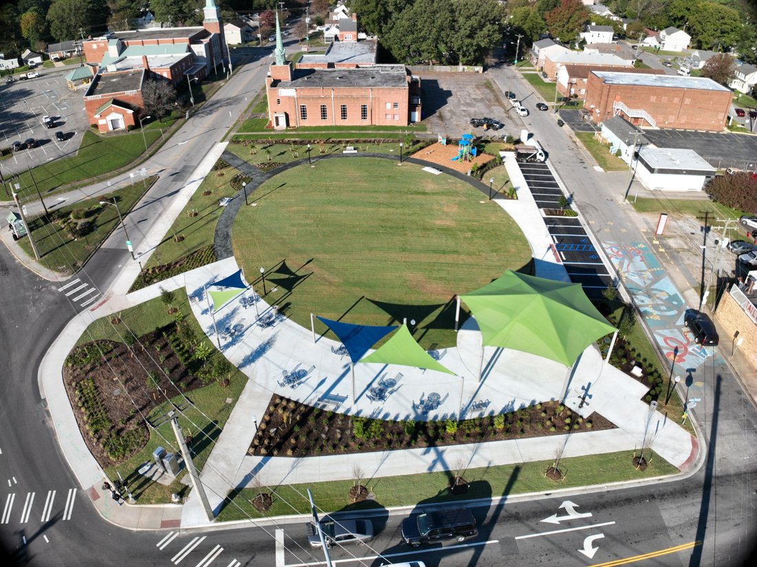 Aerial view of a neighborhood park with curved paths, lawn, play equipment, and shade structures