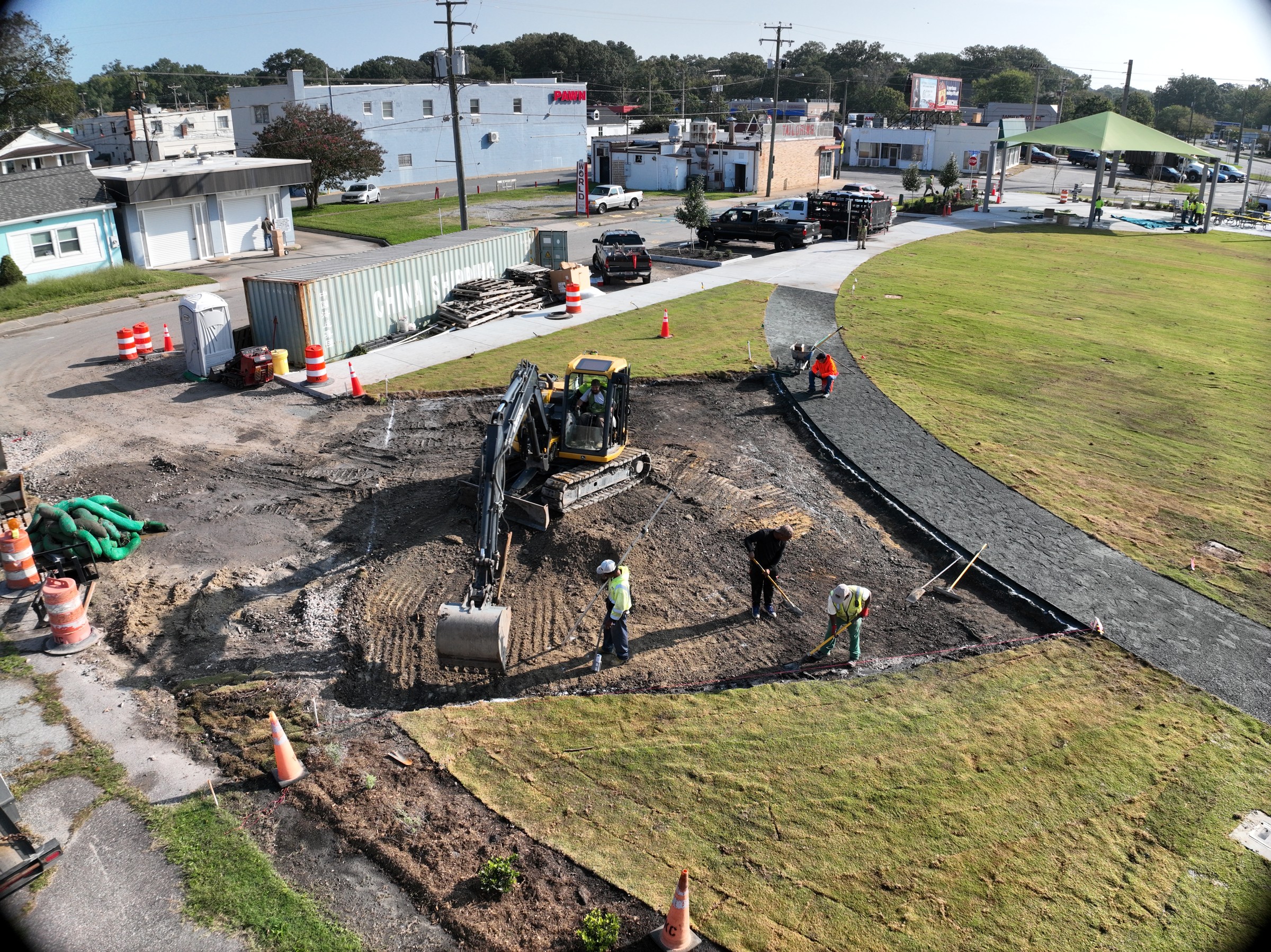 Crews shape the excavation beside the developing paths and lawn.